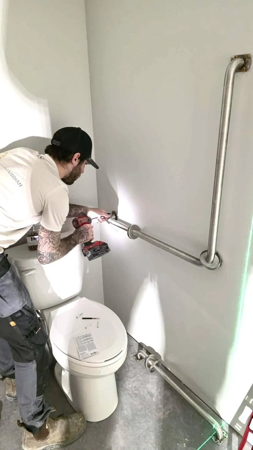 A crew member fitting a grab bar in a washroom, drill in hand
