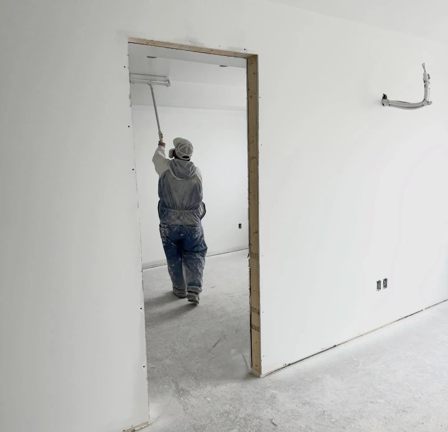 A painter rolling a ceiling in a fresh unit, seen from behind