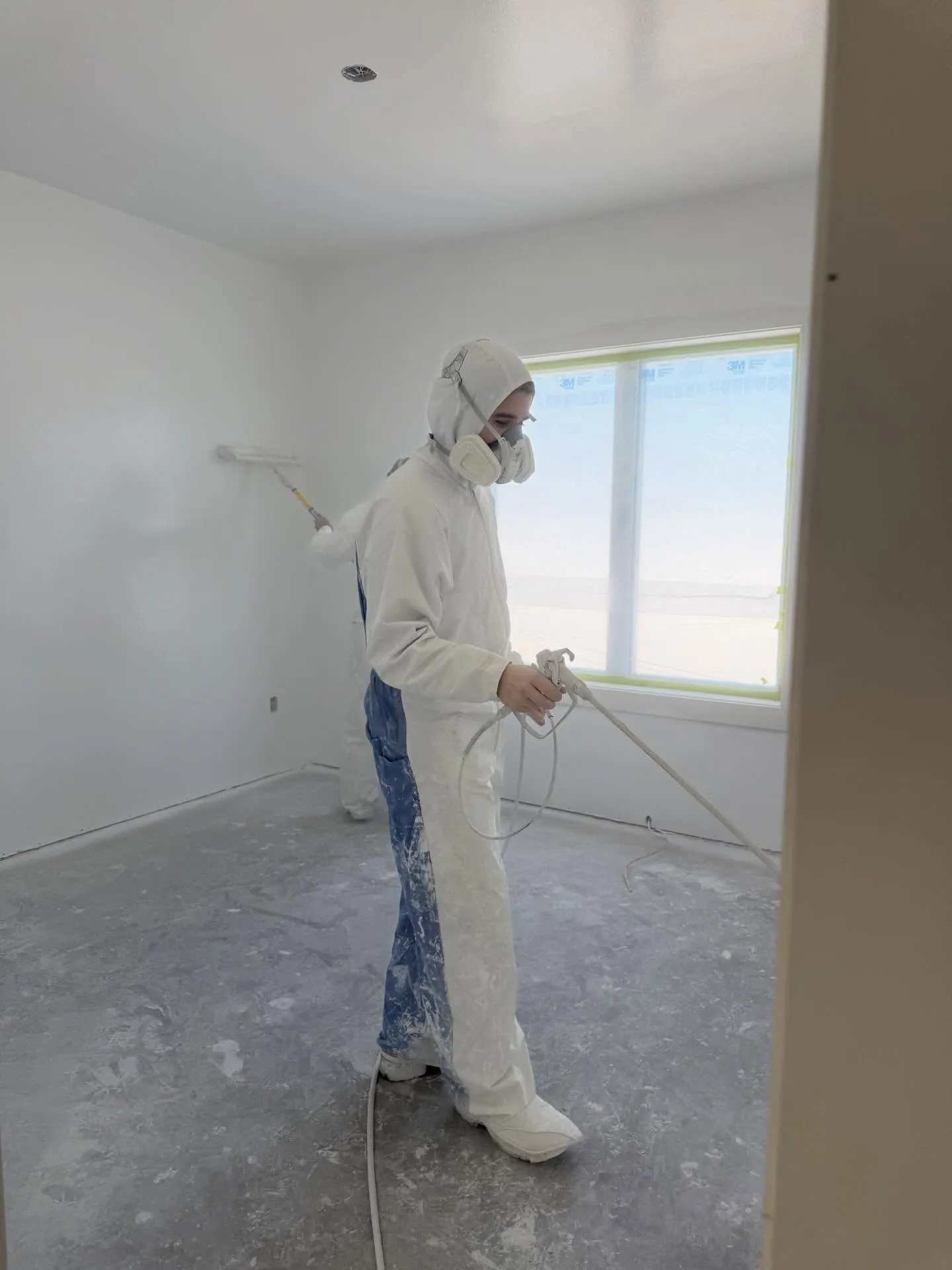 A painter in a white suit and respirator spraying a wall in an empty unit