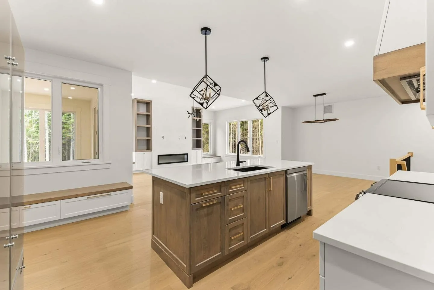 A kitchen island in stained oak with a white counter and geometric pendants