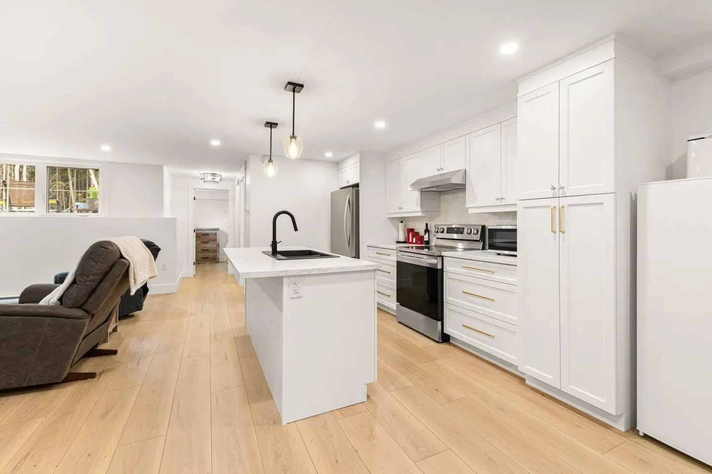A white kitchen with an island and brass pulls, oak floor running through