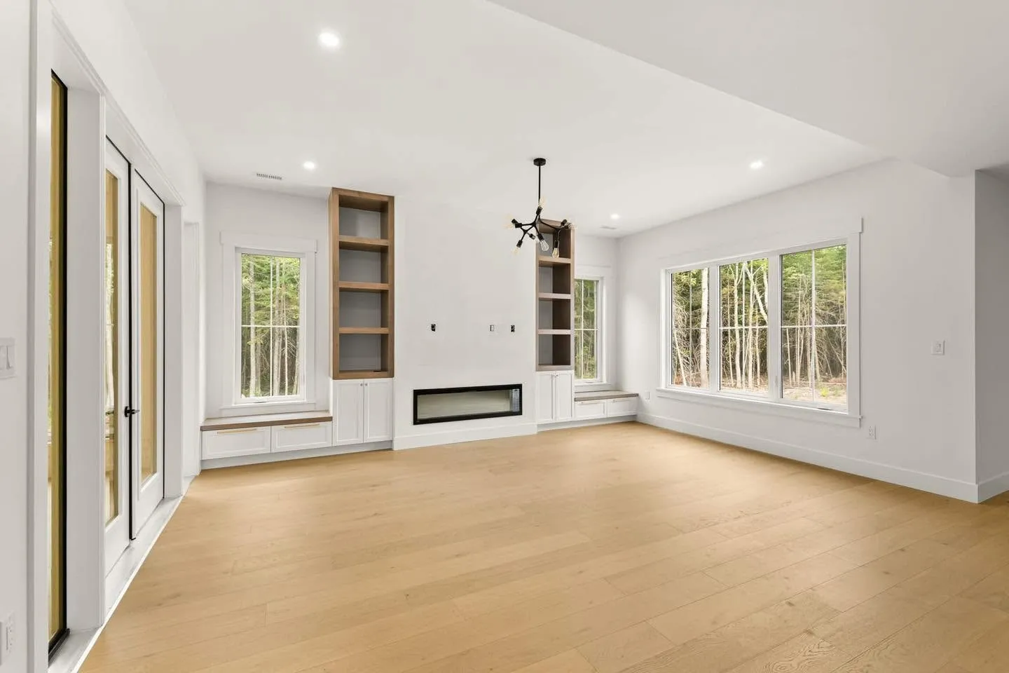 A finished living room with built-in shelving either side of a fireplace, white walls and oak floor
