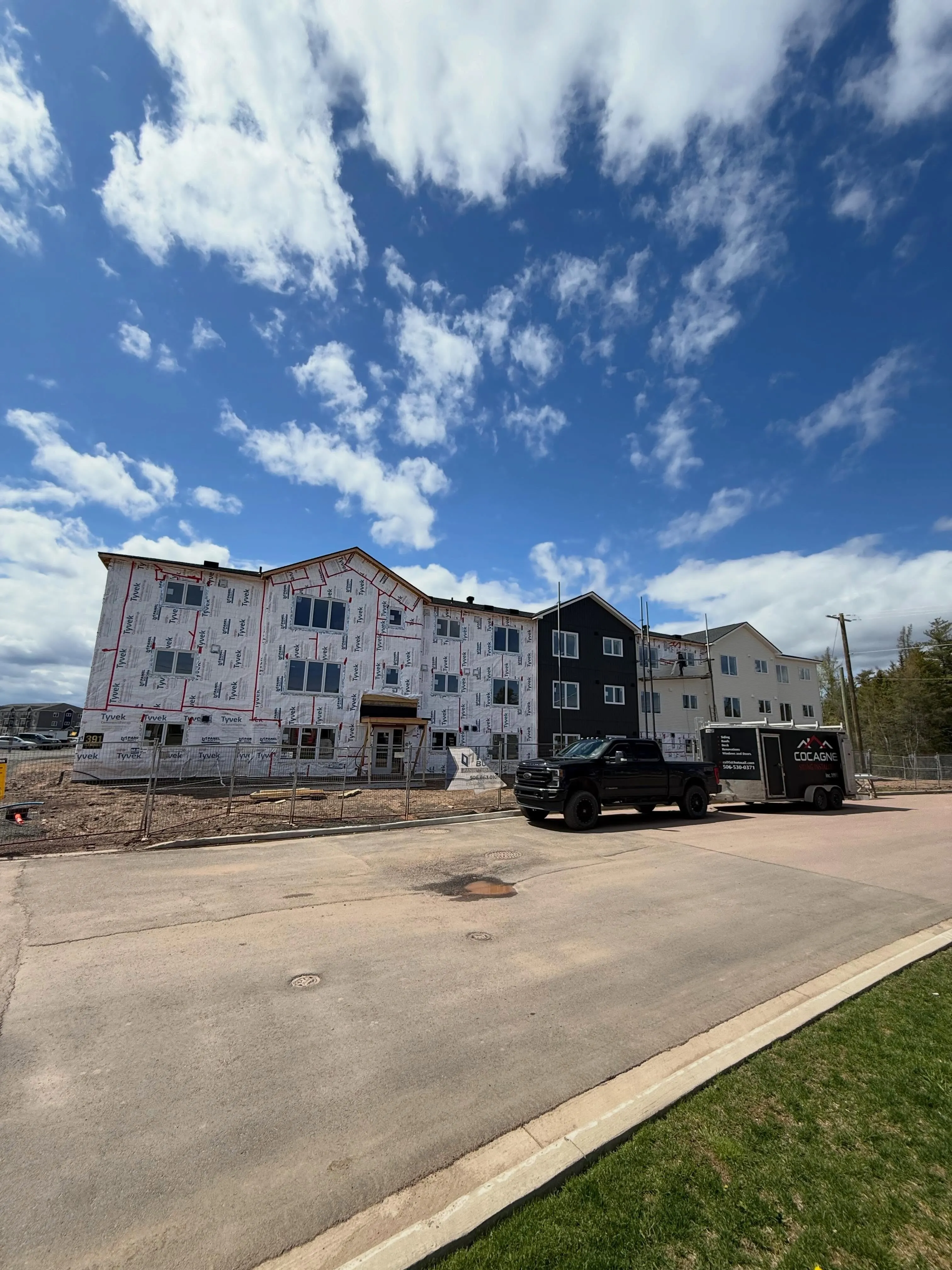 The same building from the street, wrap still on the far end, a black pickup at the door