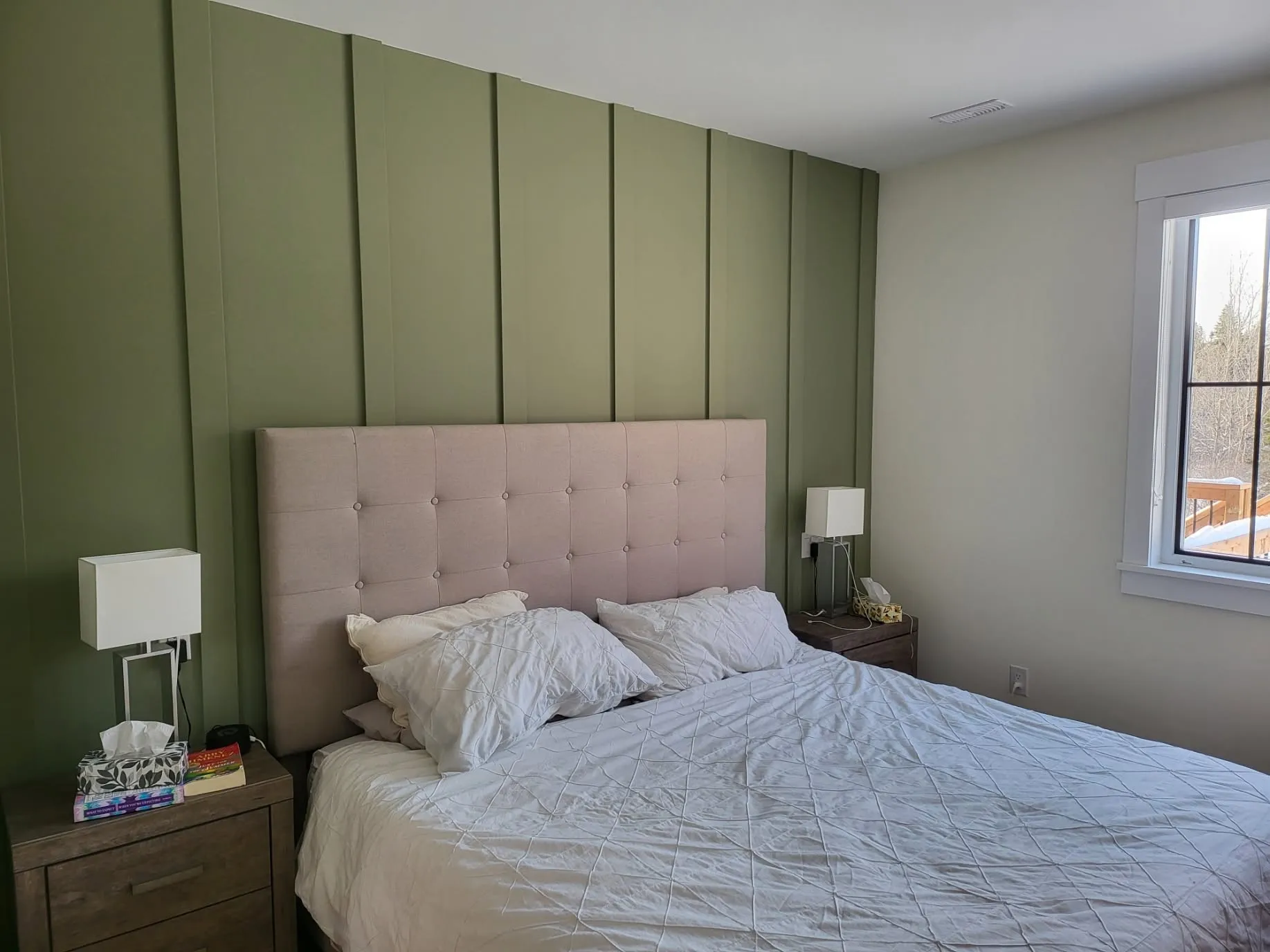 A bedroom with a deep green board-and-batten feature wall behind an upholstered bed
