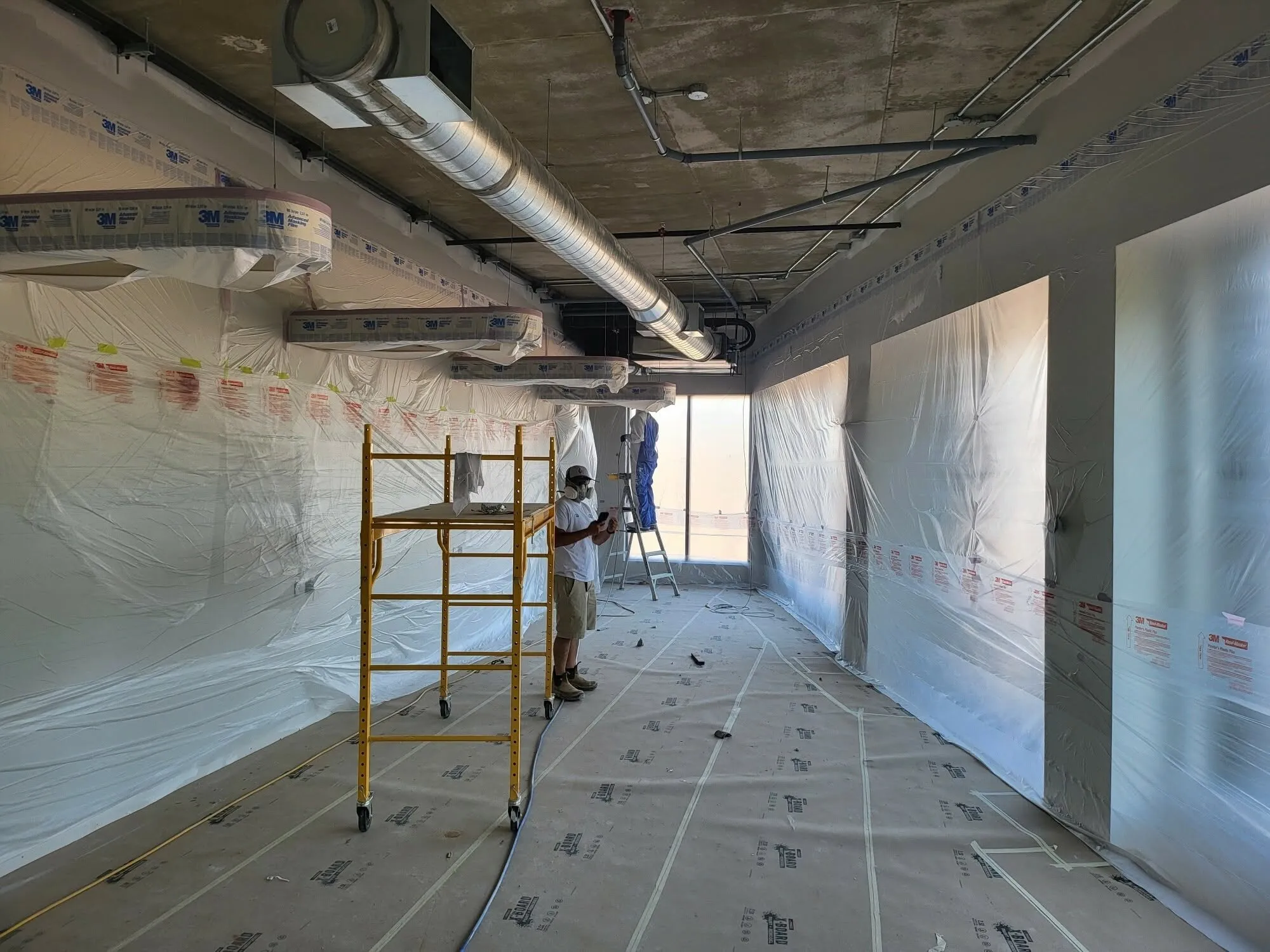 A commercial space under poly, scaffold up, ceiling being sprayed